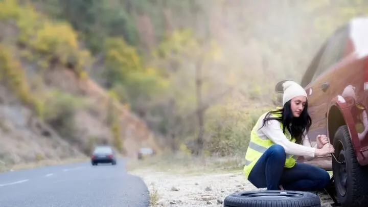 person changing flat tire on side of the road