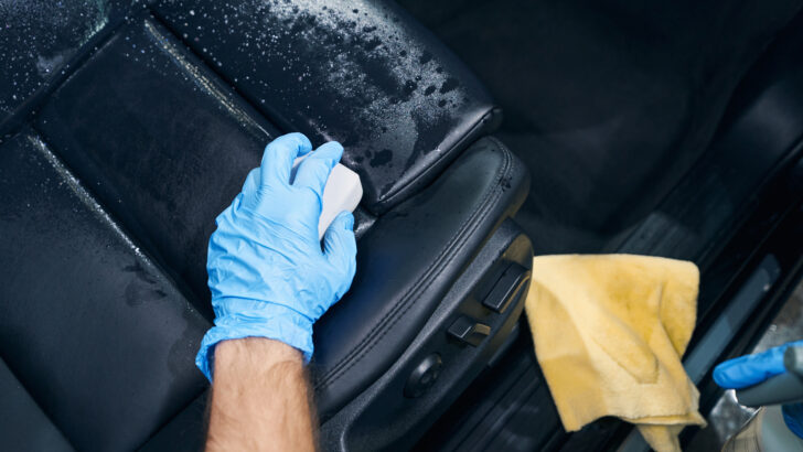 Auto service worker wiping leather car seat with sponge